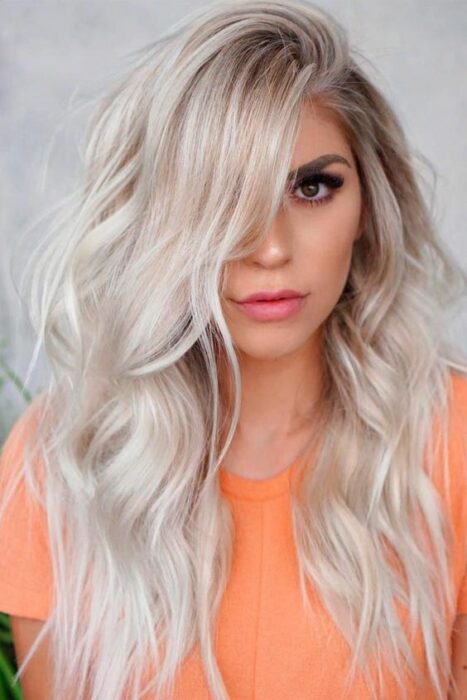 Chica con blusa naranja y cabello largo rizado en tono 'icy blonde'