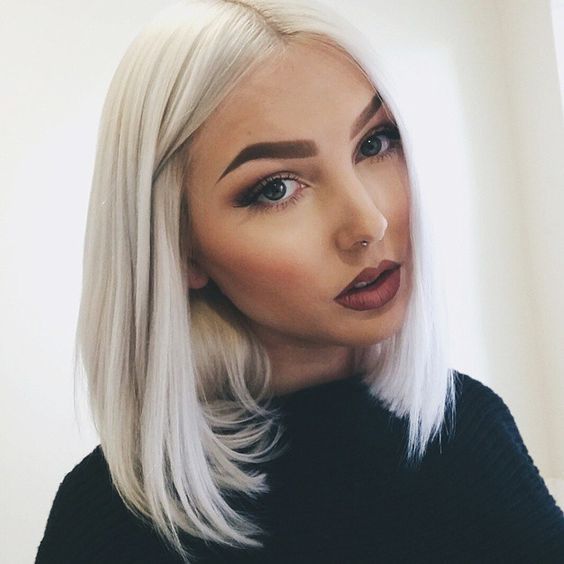 Chica de ojos azules y piercing en la nariz con melena corta y cabello lacio en tono 'icy blonde', vistiendo blusa de cuello alto negra