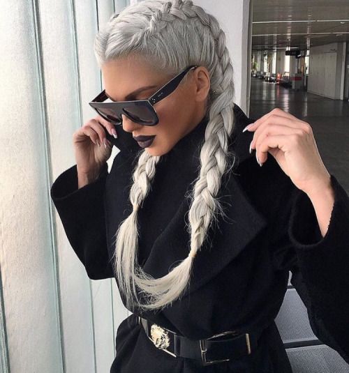 Chica con blusa y saco negros y gafas de sol cuadradas, con cabello en tono 'icy blonde' peinado en dos trenzas francesas