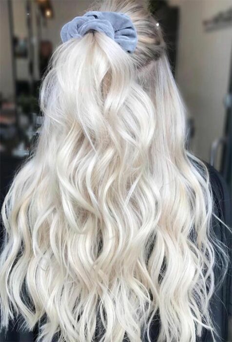 Chica de espaldas con cabello largo rizado en tono 'icy blonde', sujeto en media coleta con un scrunchie azul pastel