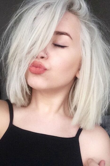 Chica blanca haciendo 'duck face' con blusita de tirantes negra y melena corta en tono 'icy blonde'