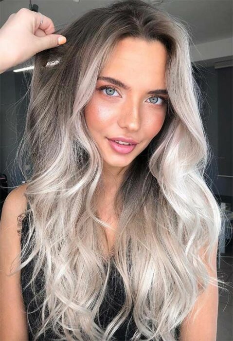 Chica de ojos verdes claros y labios rosas con blusa de tirantes negra y cabello largo degradado de café en la parte superior a blanco 'icy blonde' en las puntas