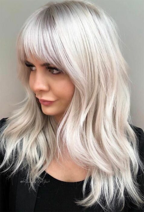 Chica con blusa negra mirando hacia un costado y melena larga cortada en capas cortas en tono blanco 'icy blonde'