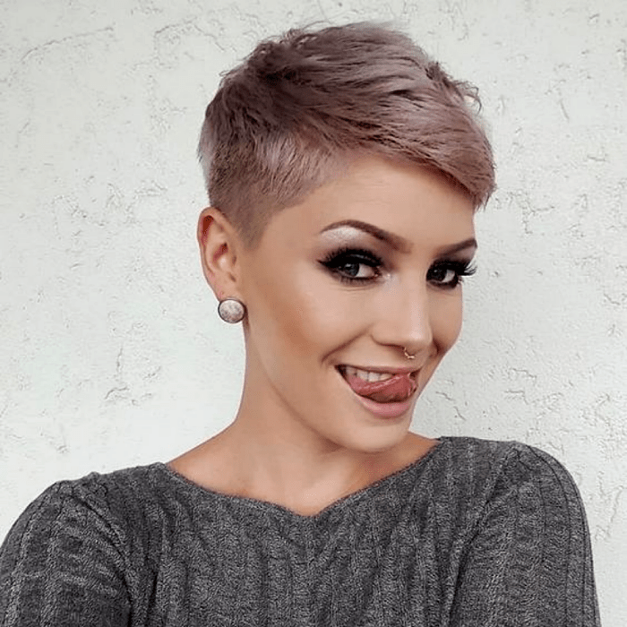 chica de cabello rosa platinado con corte de cabello pixie, top gris de manga larga
