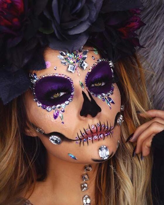 Chica con maquillaje de Catrina en colores morados con perlas y pedrería