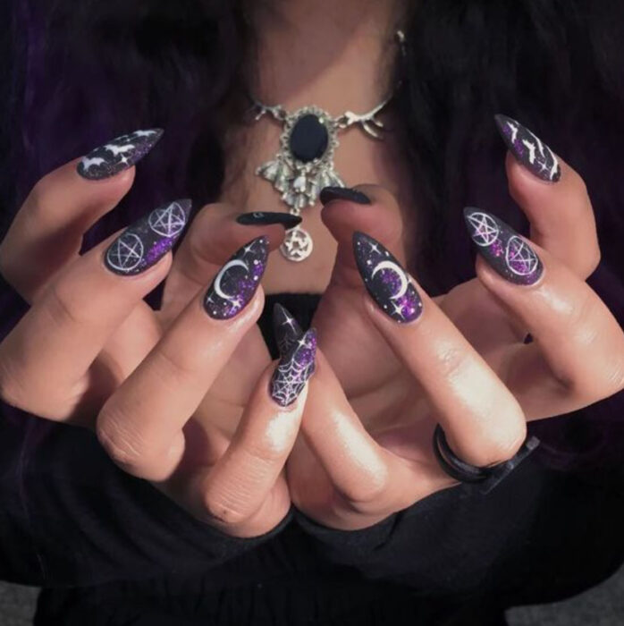 Manicura inspirada en noche de brujas de fondo negro con morado y detalles en blanco