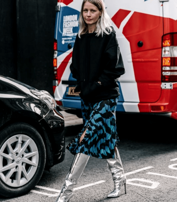 chica rubia con un top negro de manga larga, falda midi azul con líneas negras, botas largas metálicas plateadas