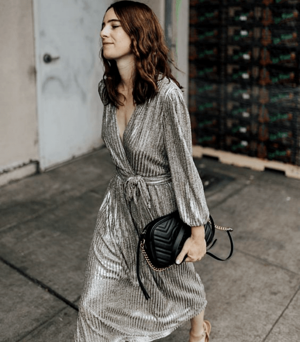 chica de cabello castaño con un vestido largo metálico plateado, bolso negro y sandalias de tacón beige