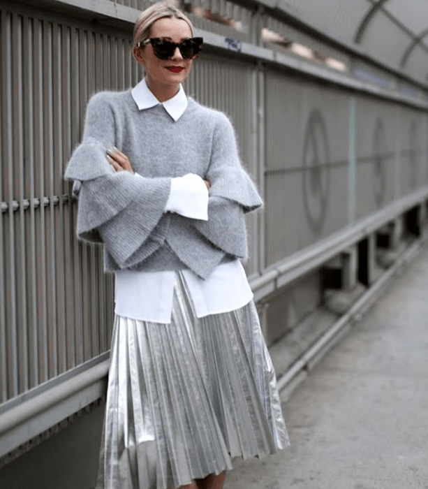 chica rubia con lentes de sol, suéter gris con mangas holgadas, camisa blanca, falda larga de tablones metálica plateada