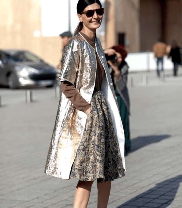 chica de cabello castaño con lentes de sol, top marrón de manga larga, abrigo largo metálico dorado claro, falda larga estampada beige