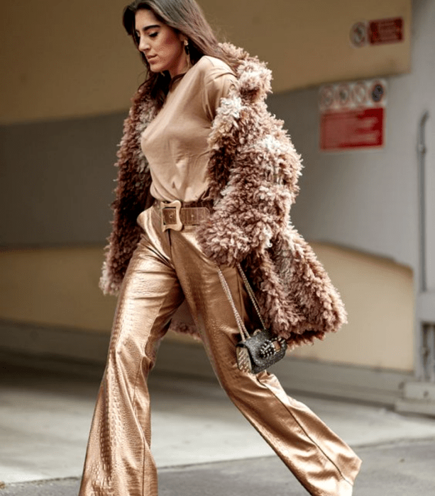 chica de cabello castaño usando un top marrón, abrigo teddy marrón afelpado, pantalones acampanados metálicos cafés y bolso café con detalles dorados