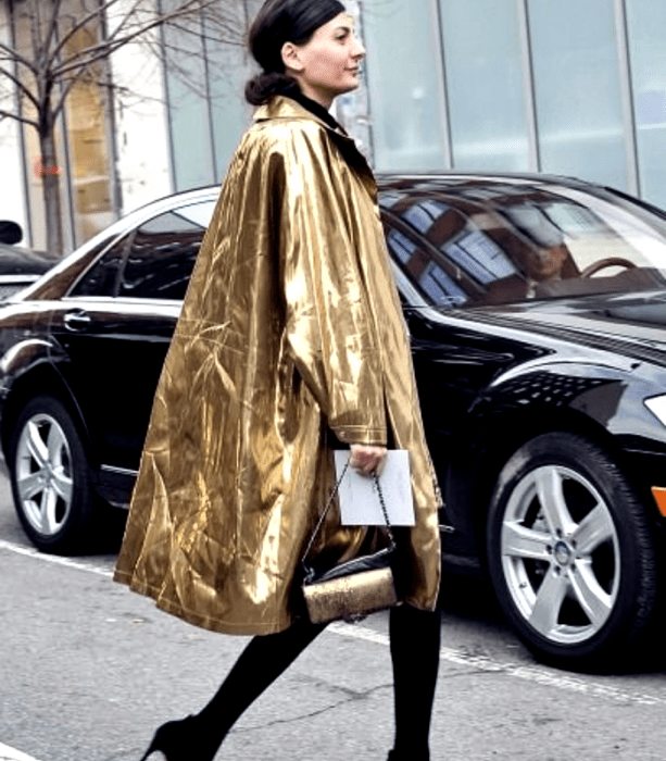 chica de cabello castaño usando un abrigo largo dorado metálico, bolso negro con detalles dorados, medias gruesas negras y zapatos de tacón negros