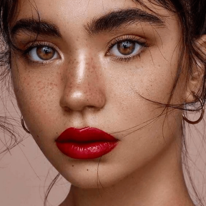 chica de ojos miel usando lipstick rojo y maquillaje natural con pecas