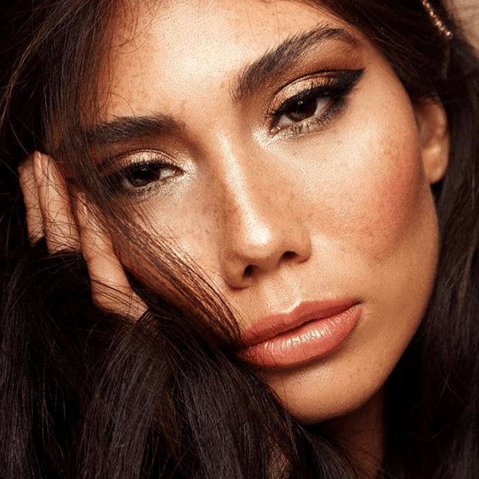 chica de cabello castaño con pecas, usando maquillaje de sombras doradas, delineador negro