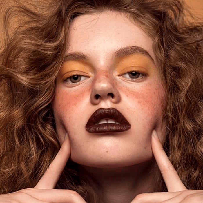 chica de cabello pelirrojo chino con pecas usando maquillaje de sombra amarilla, blush rojo, lipstick guinda