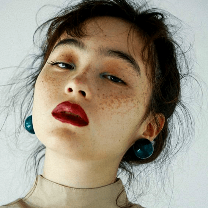 chica de cabello oscuro usando maquillaje natural, con pecas, lipstick rojo y sombra amarilla con sombra verde en el lagrimal