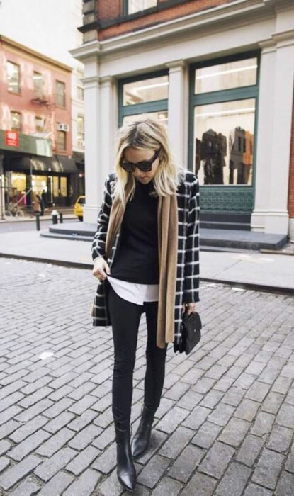 Outfit para la oficina de otoño-invierno de saco negro a cuadros, suéter negro, camisa blanca debajo, jeans y botines negros con bufanda color caki