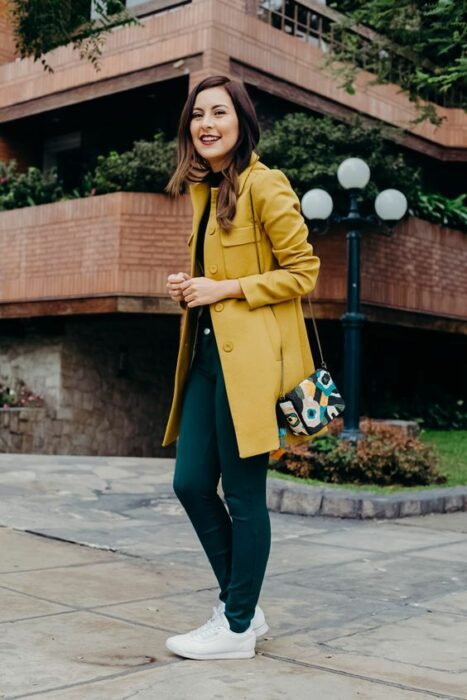 Outfit para la oficina de otoño-invierno de abrigo color mostaza, blusa y pantalón color petróleo, y zapatillas blancas