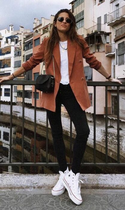 Outfit para la oficina de otoño-invierno de blazer color ladrillo, suéter blanco, jeans negros y zapatillas blancas
