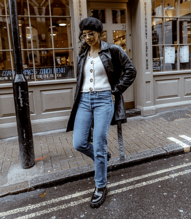 chica morena usando una boina de piel, suéter blanco, abrigo de cuero negro, jeans y botas gruesas negras