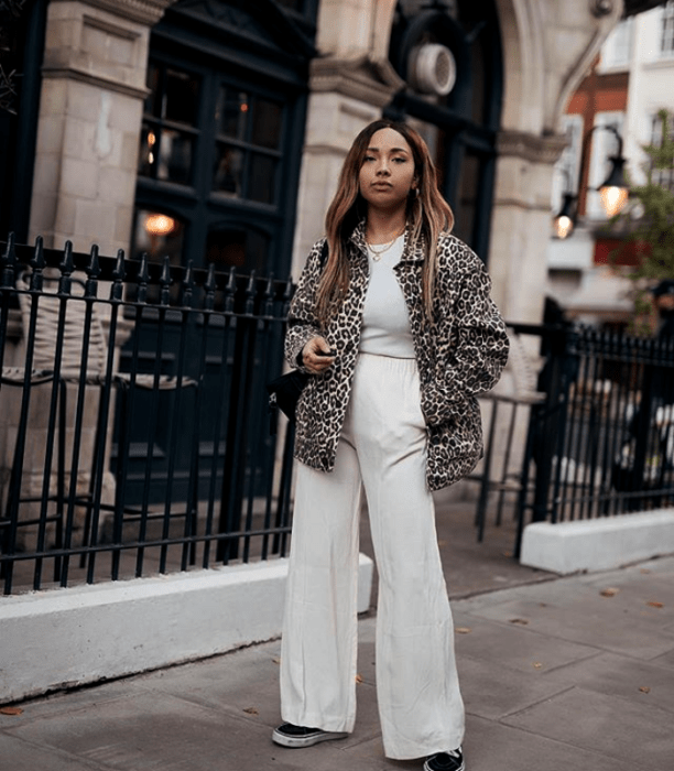 chica morena usando un abrigo de animal print, top blanco y pantalones acampanados blancos