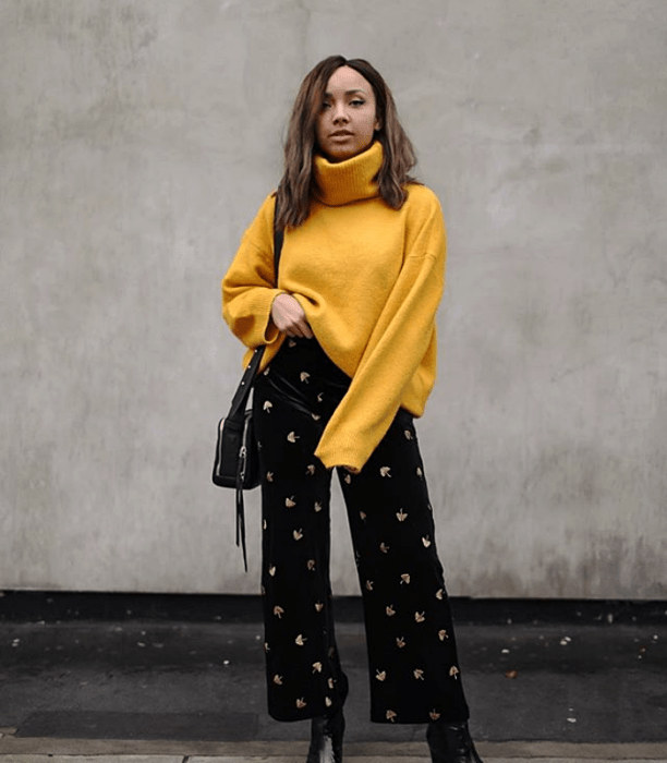 chica morena usando un suéter amarillo de cuello alto, pantalones acampanados de pana con estrellas y bolso negro