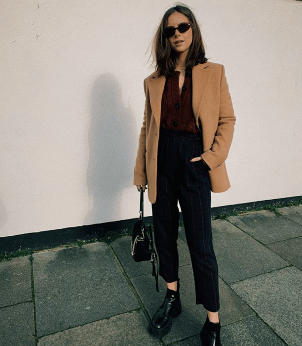 chica de cabello largo castaño usando un blazer beige, top guinda, pantalones de vestir, bolso pequeño de cuero y botines negros de cuero
