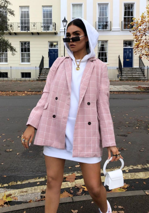 Looks con sudadera; mujer caminando en la calle con hoodie blanco como vestido, saco rosa con cuadros, bolsa pequeña blanca y lentes de sol rectangulares