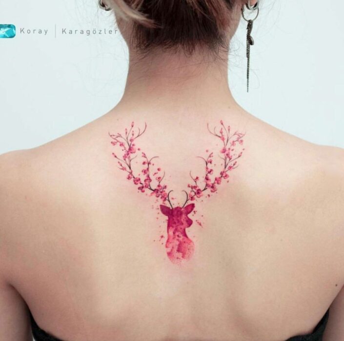 Chica con un tatuaje de color rosa en forma de venado con flores en sus cuernos