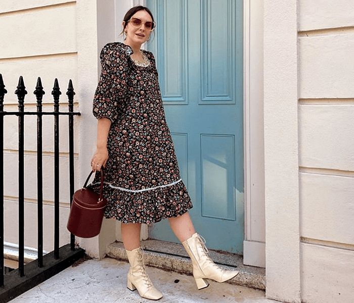 chica de cabello castaño usando un vestido midi oscuro de flores y mangas abombadas, botines blancos de piel con tacón y bolso café bucket bag
