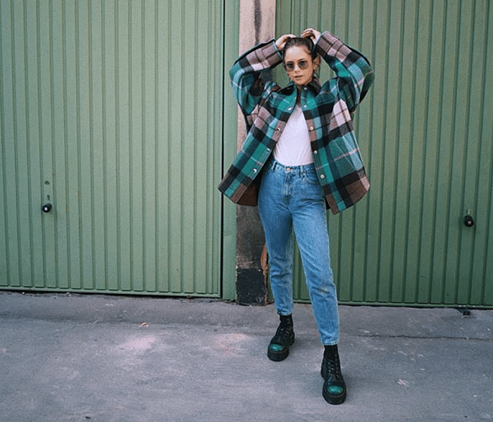 chica de cabello castaño usando lentes de sol, top blanco, chaqueta de cuadros azules con gris, jeans y botas dr. marten verdes