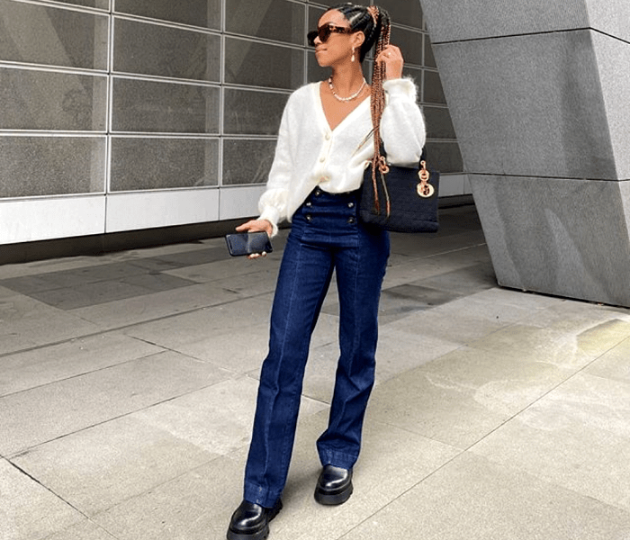 chica morena con cabello claro usando un cárdigan blanco de manga larga, jeans a la cintura, botines negros de plataforma gruesa y bolso negro