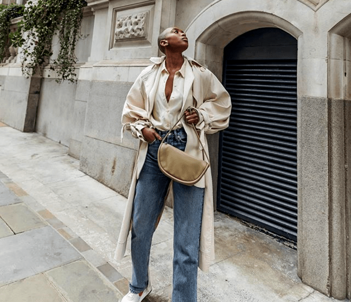 chica morena con blusa beige de satén, abrigo largo beige, jeans a la cintura tipo mom jeans, tenis blancos y bolso de mano café claro