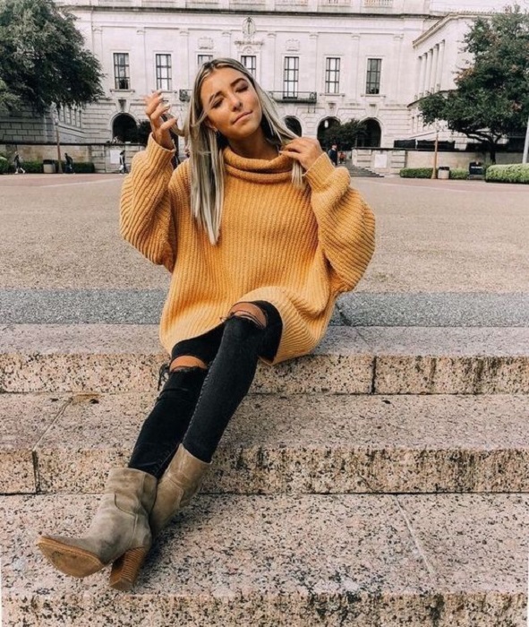 Chica usando suéter holgado color mostaza, jeans rasgados y botines color gris