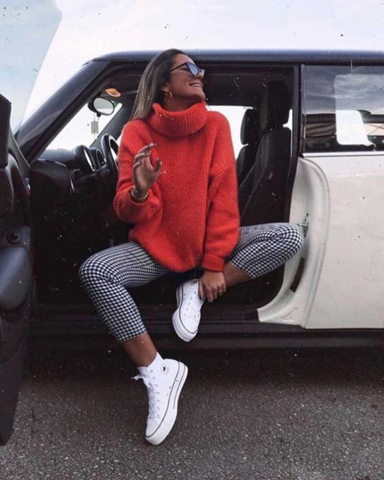 Chica usando suéter holgado color rojo con pantalón tartán y converse blancos