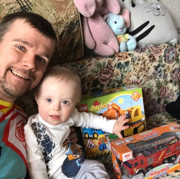Papá jugando junto a su pequeño con síndrome de Down mientras están sentados en un sofá 