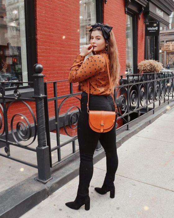 Chica curvy usando jeans con botines negros, vestido y bolso color ladrillo