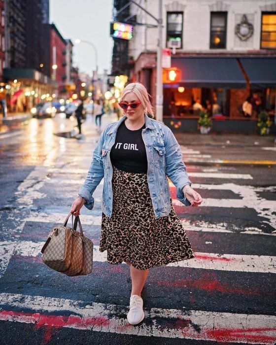Chica curvy usando tenis blancos, falda maxi de estampado animal print, camiseta negra y chaqueta denim