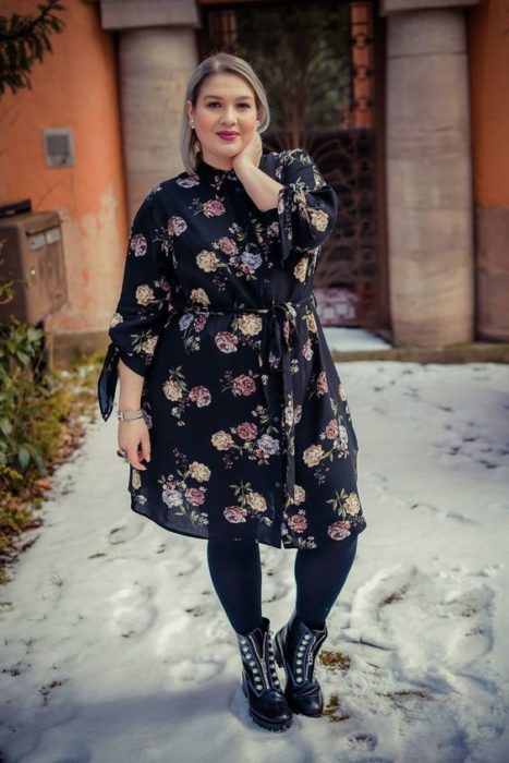 Chica curvy usando medias y botines negros con vestido de manga larga negro y estampado floral