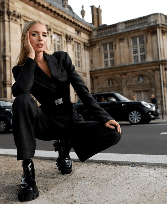 Chica rubia usando traje formal negro, blazer negro, cinturón negro, pantalones de vestir negros y botines negros de plataforma