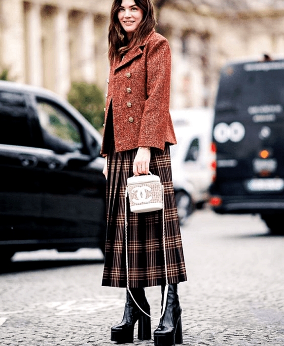 Chica de cabello castaño usando abrigo rojo con botones dorados, falda maxi de cuadros y botas de plataforma negras