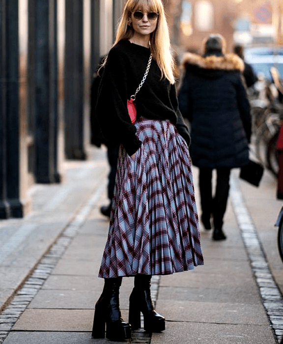 Chica rubia usando lentes de sol, suéter negro, falda maxi azul con botas de plataforma
