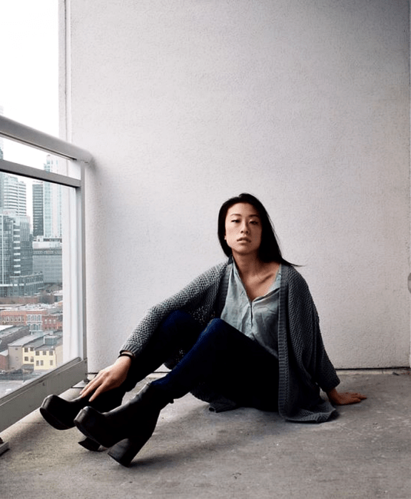 Chica de cabello negro usando camisa gris, cárdigan gris, skinny jeans y botines negros de plataforma