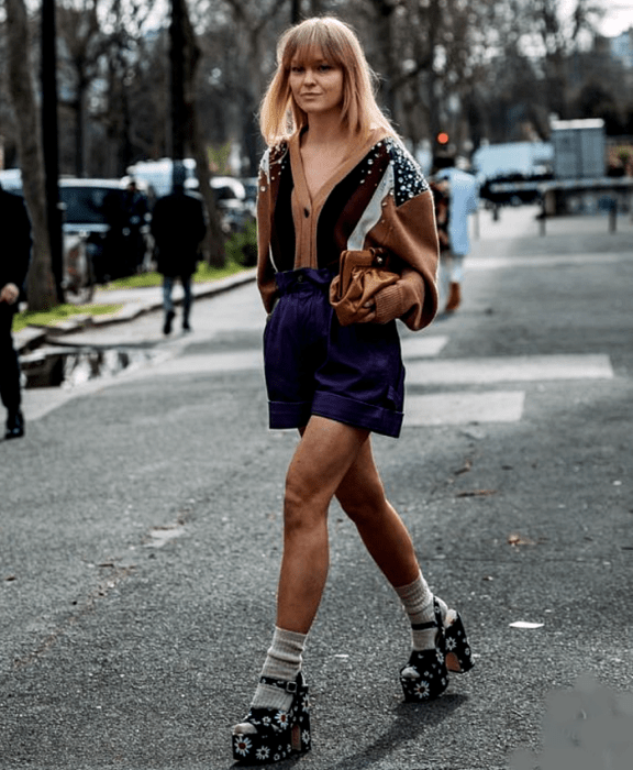 Chica rubia usando cárdigan con líneas, shorts azul marino y sandalias de plataforma decoradas