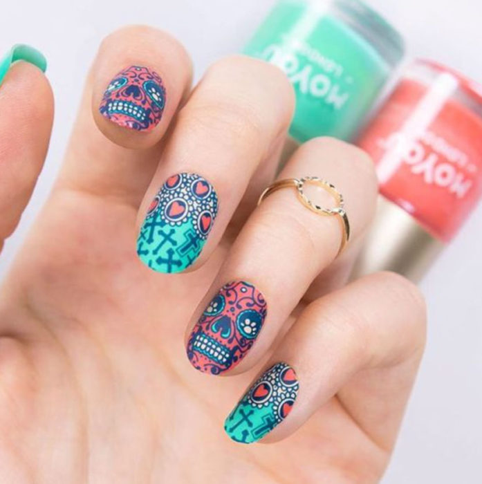 Uñas inspiradas en Día de Muertos con diseño de calaveras, en colores fucsia y verde