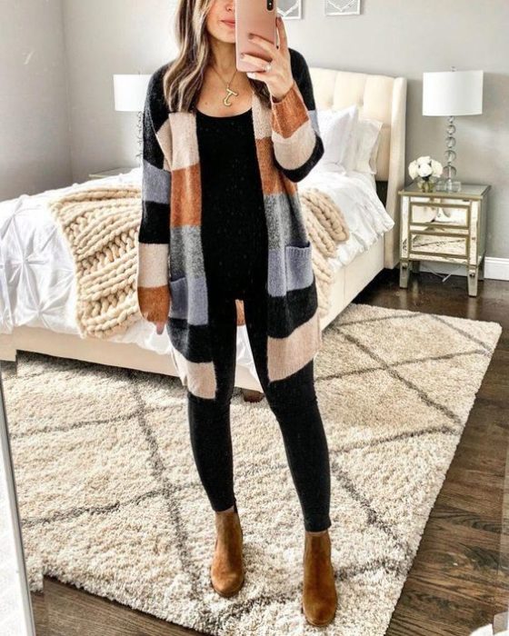 Chica usando jeans negros, top negro, botines camel y suéter largo de rayas de varios colores