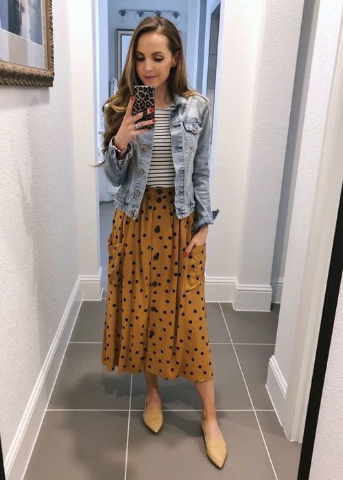 Chica tomándose un selfie frente a un espejo con maxi falda amarilla con puntos negros, blusa de rayas blanca y negra y chaqueta de mezclilla