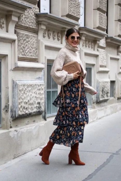 Chica posando con suéter de cuello de tortuga gris y maxi falda azul marino con flores y botines color burdeos