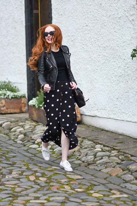 Chica pelirroja con blusa, chaqueta y falda negras con bolitas blancas
