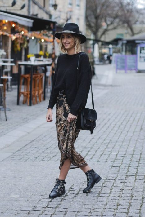 Chica rubia caminando por la calle con sombrero negro, suéter negro, botines negros y maxi falda de leopard print